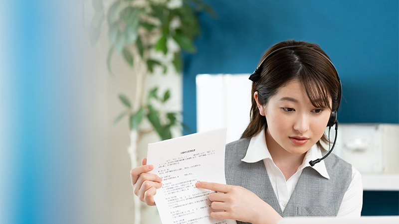 ヘッドセットを着けた女性が、手に持っている書類について何かを説明しています。