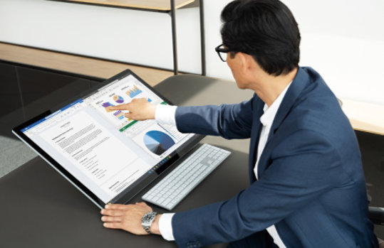  オフィスで高解像度の 28 インチ大画面ディスプレイ Surface Studio 2+ を手動で操作する男性