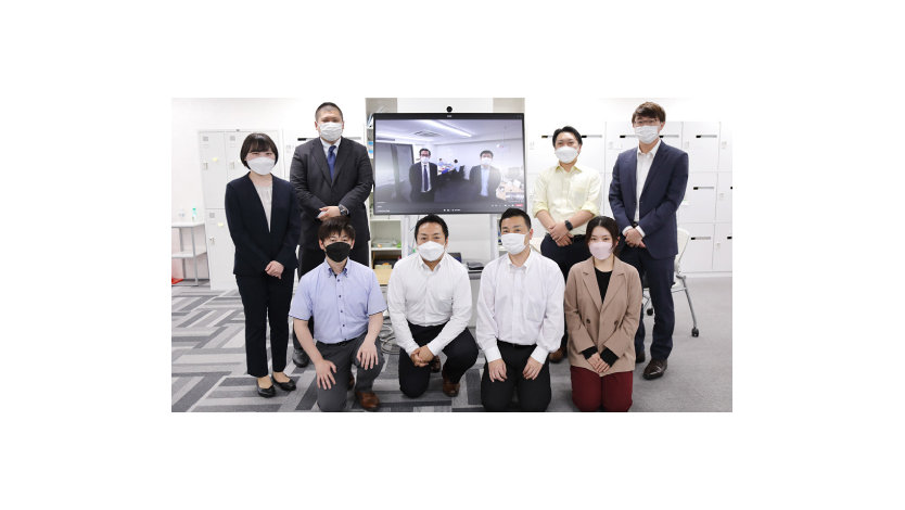 大型モニターの前でポーズをとる株式会社レンタルバスターズのスタッフ8名