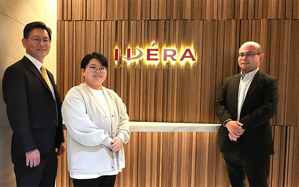 3人が木製の壁の前に立ち、背後に発光する「IDERA Capital Management」のサインがある