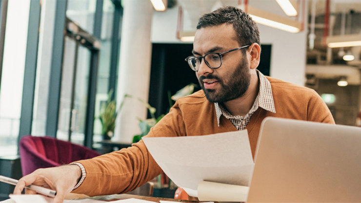 Person sitting at a desk looking at papers and a laptop