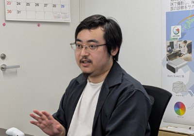 眼鏡をかけた男性が、両手を広げて親しげに話している。