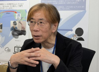 メガネをかけ明るい髪色の男性が、手を組んで真剣な表情で話す様子。