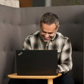 Ein Mann sitzt an einem kleine Tischchen, vor ihm ein aufgeklappter Laptop