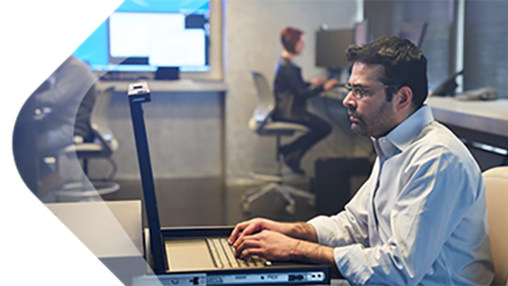 Ein Mann mit Brille arbeitet vor Desktop-Bildschirmen.