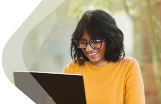 Eine lächelnde Frau im gelben Pullover schaut auf einen Laptop