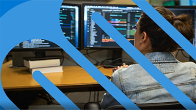 Frau in Jeansjacke sitzt vor mehreren Bildschirmen.