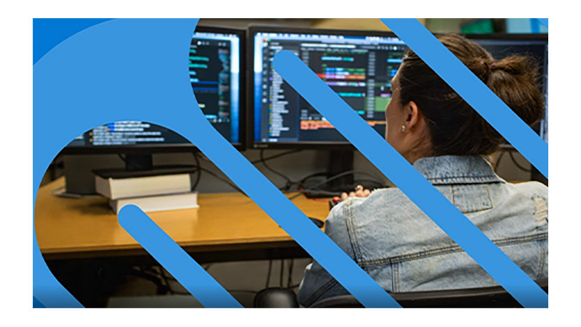 Frau in Jeansjacke sitzt vor mehreren Bildschirmen.