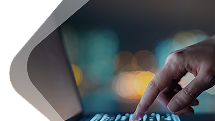 Seitliche Aufnahme einer Hand, die auf der Tastatur eines aufgeklappten Laptops tippt.