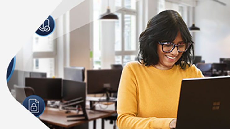 Eine Frau im gelben Pullover schaut lächelnd auf einen PC-Bildschirm.