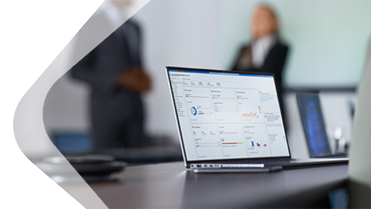 Ein Laptop steht auf einem Tisch, während im Hintergrund zwei Personen angedeutet sind.