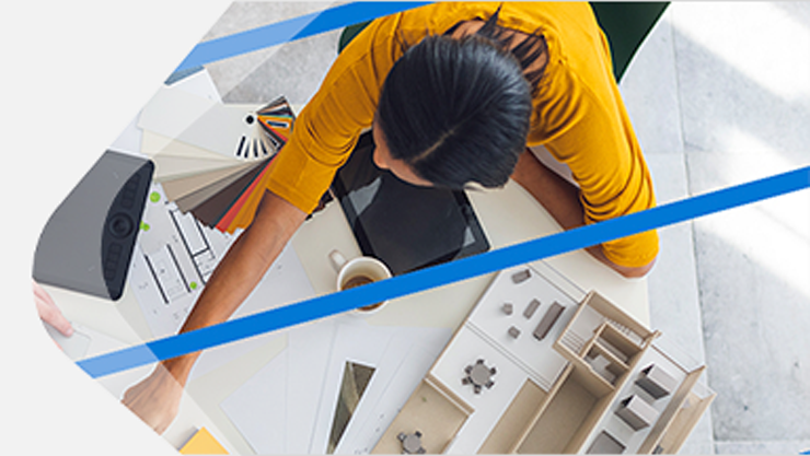 Eine Frau ist über einem Schreibtisch gebeugt, auf welchem ein Laptop und mehrere Schreibutensilien stehen.