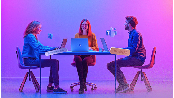 Drei Personen sitzen an einem Tisch in farbigem Studio‑Setting und arbeiten gemeinsam mit Laptops,  umgeben von digitalen Symbolen.