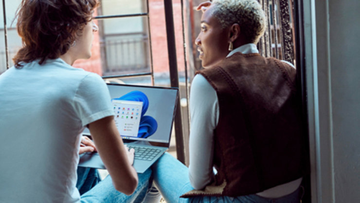 Zwei Personen sitzen mit einem Laptop am Fenster