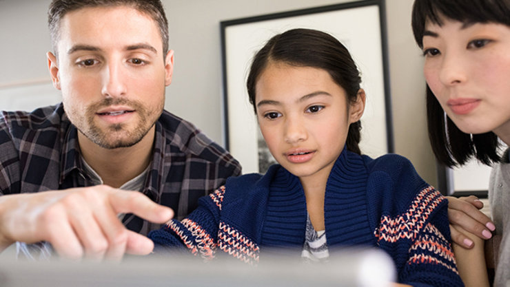 Ein Mädchen blickt mit ihren Eltern auf einen Laptop.