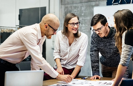 In einem Konferenzraum arbeiten 4 Personen zusammen an einem Tisch