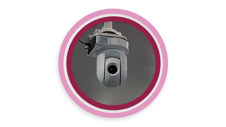 In einem rot-rosa Kreis ist eine Kamera abgebildet die an der der Decke hängt