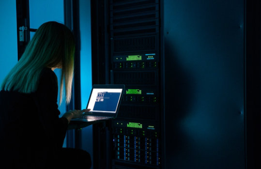 Φωτογραφία Cyber Security. Γυναίκα  τεχνικός μπροστά από Server πραγματοποιεί ρυθμίσεις.