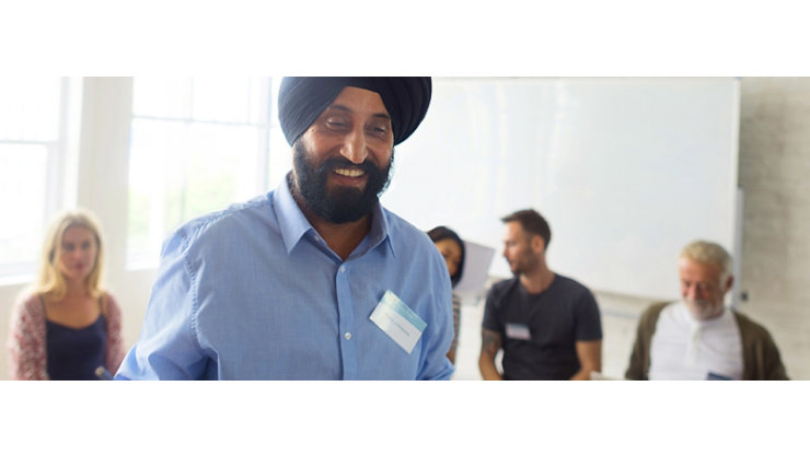 A man smiles at the camera holding a planner in front of a group