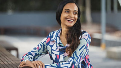 A lady wearing a shirt sitting at a bench and smiling