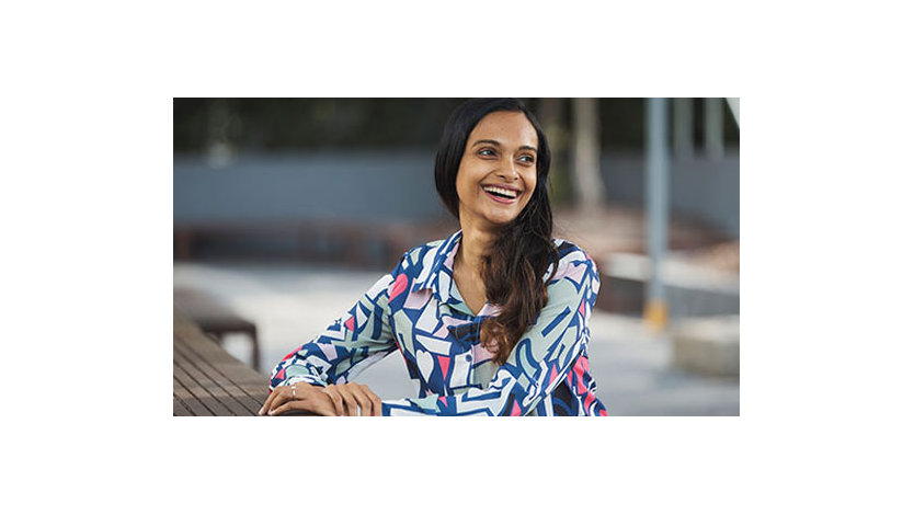 A lady wearing a shirt sitting at a bench and smiling