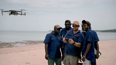 A group of people standing on a beach testing a drone 