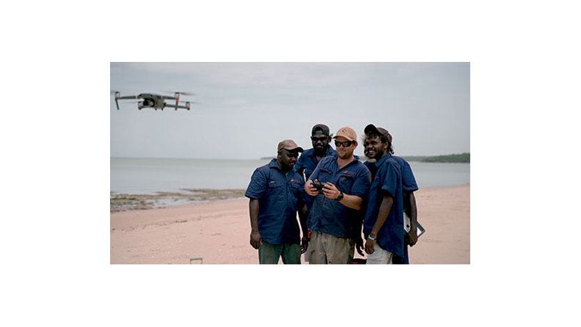 A group of people standing on a beach testing a drone 