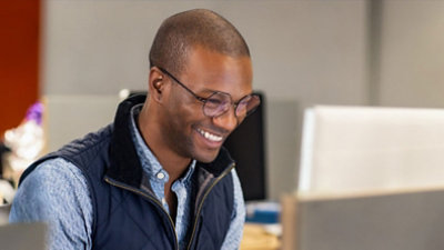 A man wearing glasses is looking downwards and smiling