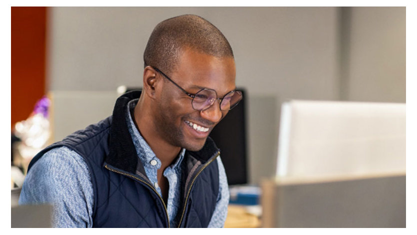 A man wearing glasses is looking downwards and smiling