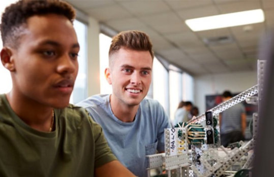 Two students in a robotics lab working on a laptop