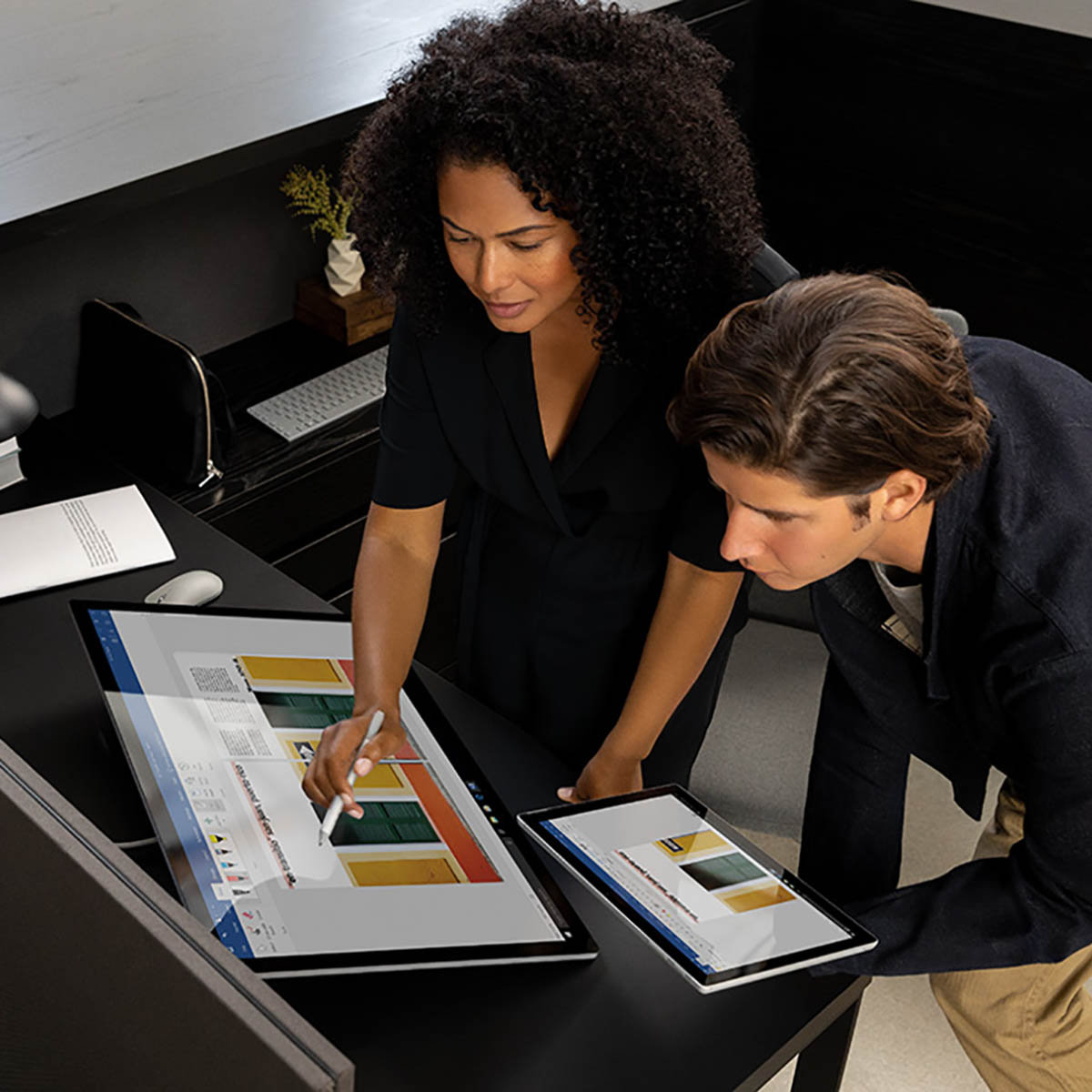 A male and female looking over their work on two tablet devices