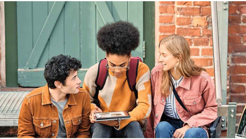 Three young people viewing a tablet device whilst sitting on steps