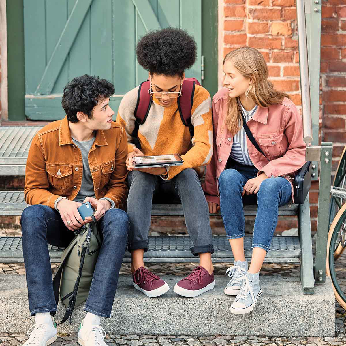 Three young people viewing a tablet device whilst sitting on steps