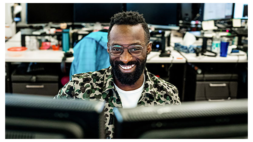 image of a smiling man sitting in front of two computer screens at an office.