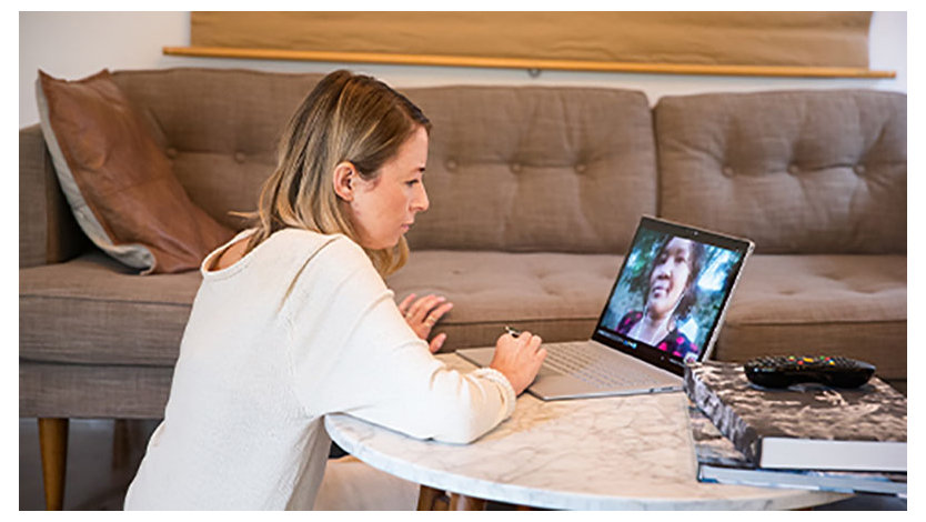 A photo of a woman sitting on the floor behind a coffee table and having a virtual meeting on her laptop