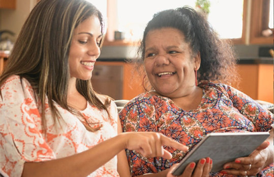 two women using technology and smiling with tab in hand.