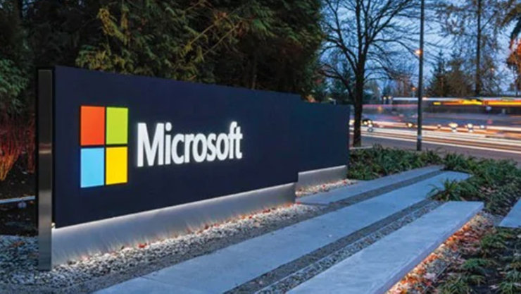 Une enseigne Microsoft illuminée au crépuscule, mettant en valeur le logo Microsoft coloré sur un fond noir.