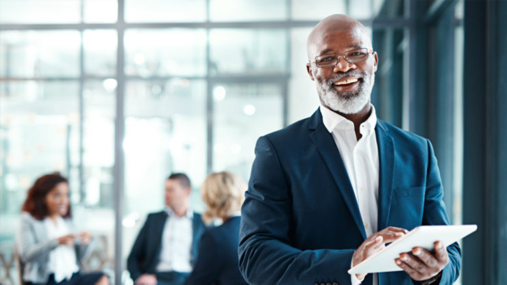 Un cadre masculin tenant une tablette et sourit en regardant la caméra.