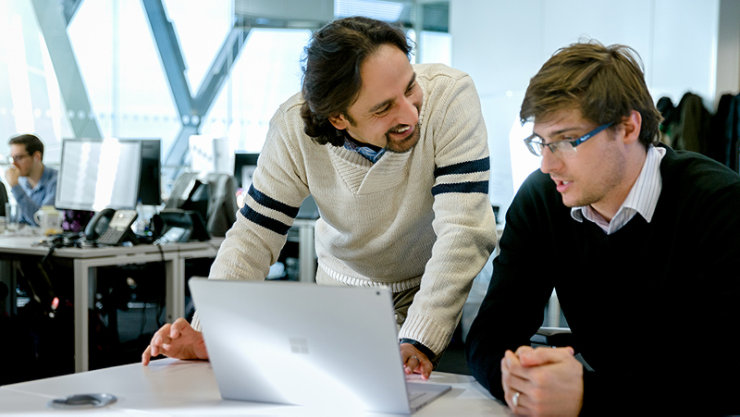 Un cadre masculin démontrant un détail de travail à l'écran à un autre cadre masculin avec le sourire