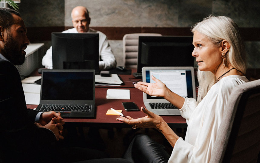 Two co-workers sitting at a business desk and talking