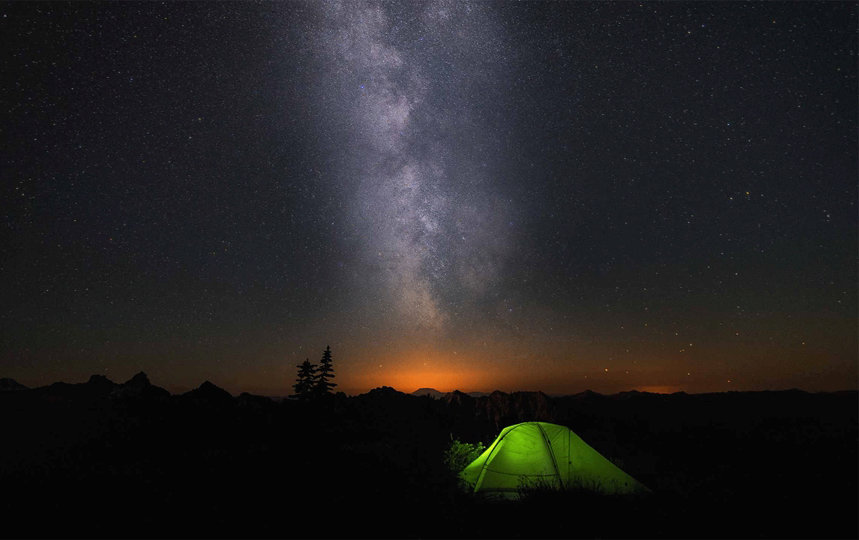 A green tent below the Milky Way in a dark night sky