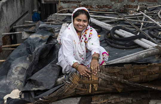A woman sitting on the roof of her tin shack home displaying a low-cost solution for keeping her house cool