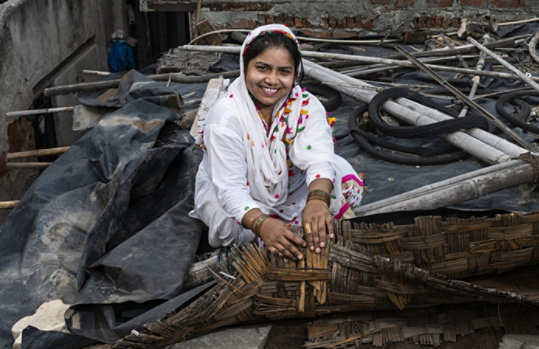 A woman sitting on the roof of her tin shack home displaying a low-cost solution for keeping her house cool