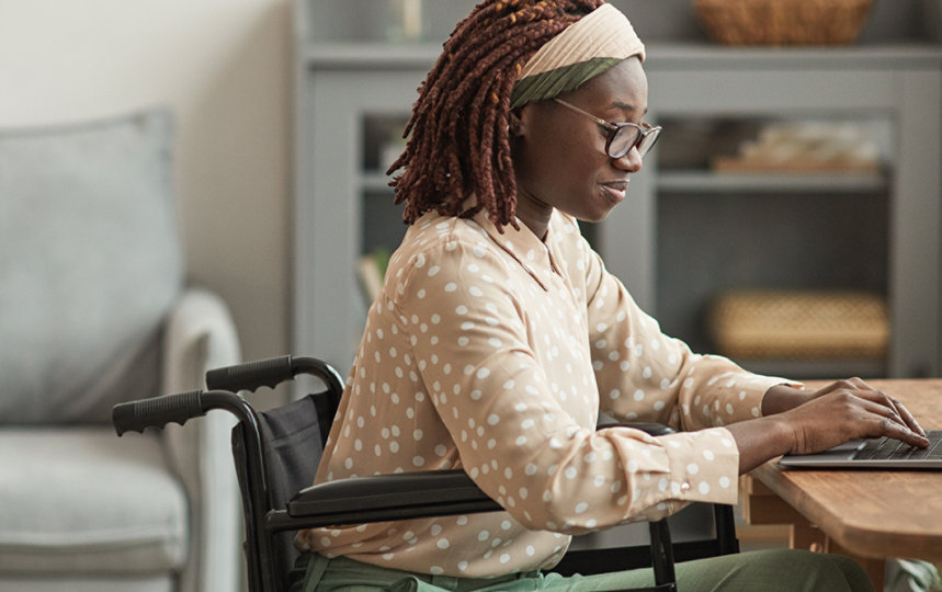 Young woman using wheelchair works on a laptop in her home office