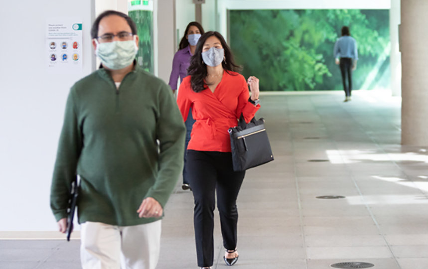 Male and female employees wearing masks walking inside a campus building