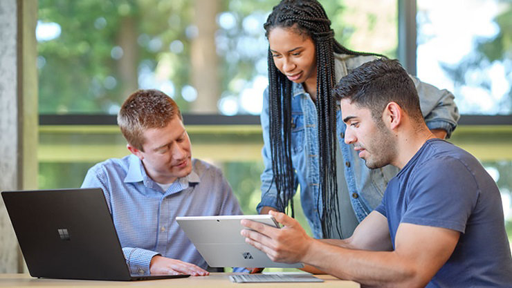 A matte black Laptop 4 is open on a desk. One student is holding a platinum Pro 7+ while another student points to the screen.