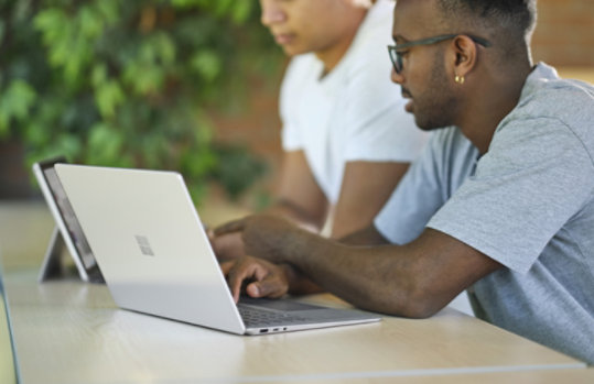 Two students are working on devices. A platinum Laptop Go is in the foreground.