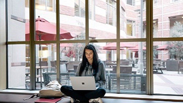 A girl sits by a window using a laptop