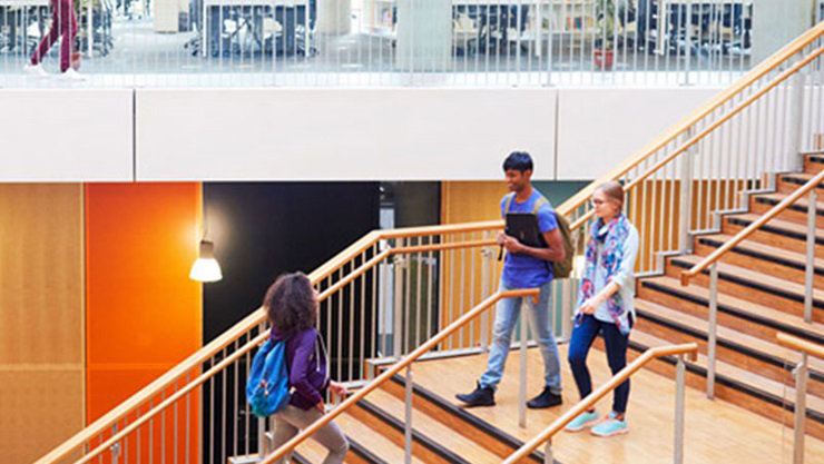 Education Color Photo of students walking on staircase with books in background on second story