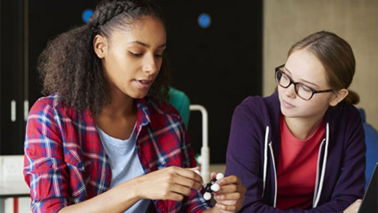 Color Photo of two female students with Surface and laptop on desk and holding molecular models.